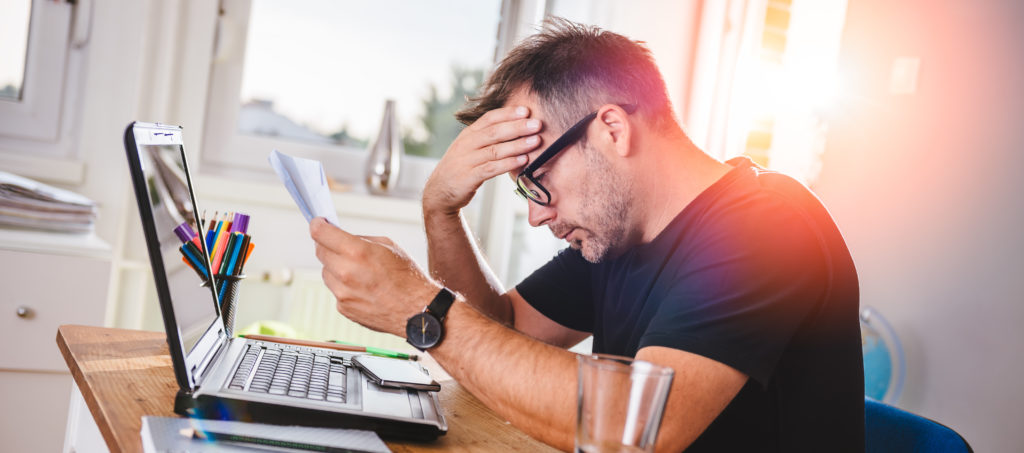 Vater sitzt vor Laptop und zerbricht sich Kopf über einen Antrag